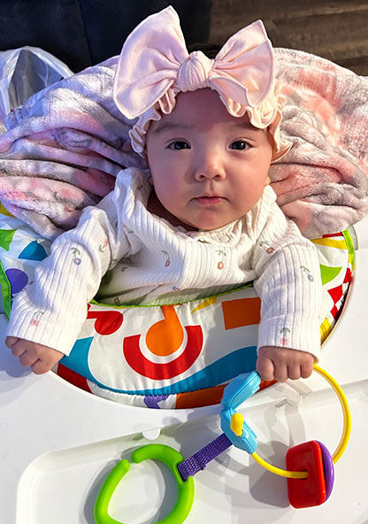 Baby Novalynn is sitting in her bouncy chair at home after recovering from a premature birth. She is happy and healthy.