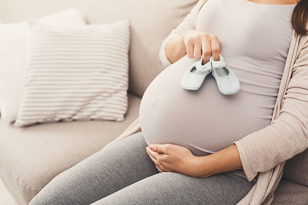 Pregnant woman holding tiny shoes near belly